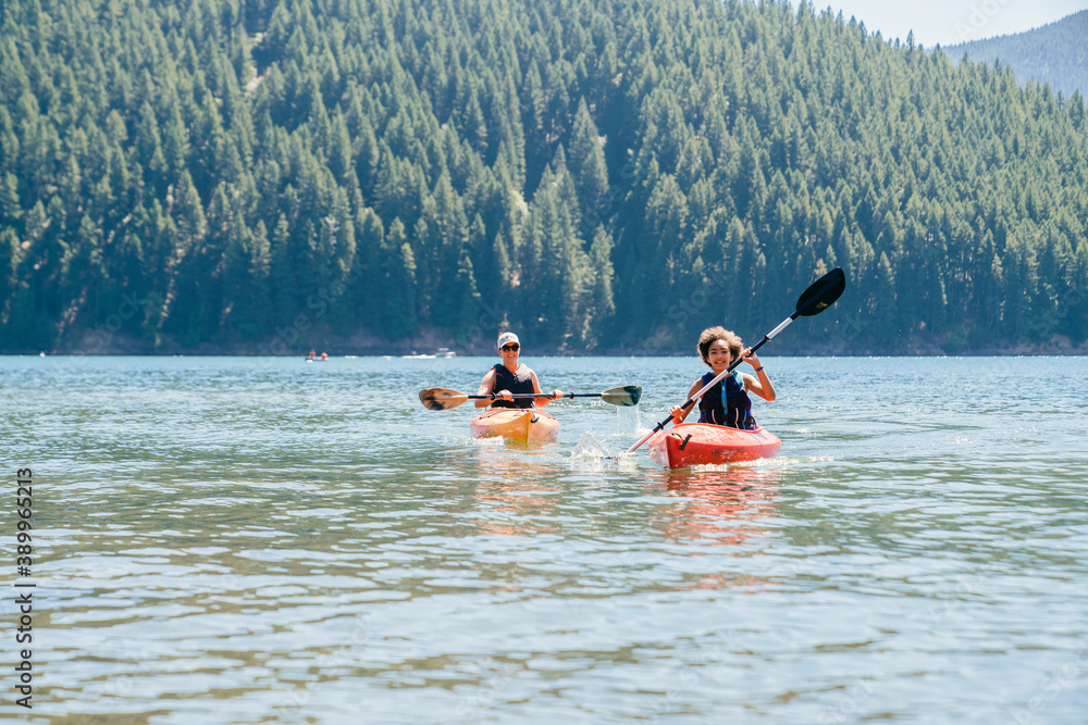 Mother and daughter paddling kayak on lake in forest in summer