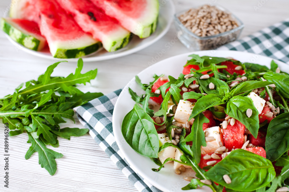 Fresh delicious salad with watermelon, feta cheese, basil leaves, arugula and peeled Sunflower seeds on white plate. Healthy food concept. Close-up. Fresh delicious salad with watermelon, feta cheese, basil leaves, arugula and peeled Sunflower seeds on white plate. Healthy food concept. Close-up.