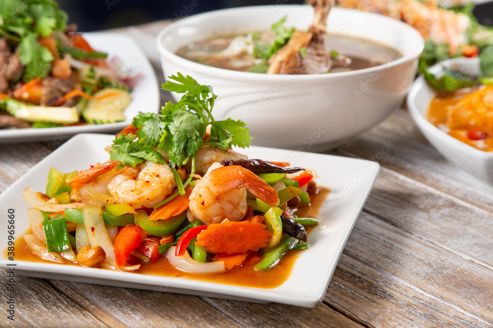 A view of several Thai dishes on a wooden table surface, featuring a shrimp cashew salad entree. A view of several Thai dishes on a wooden table surface, featuring a shrimp cashew salad entree.