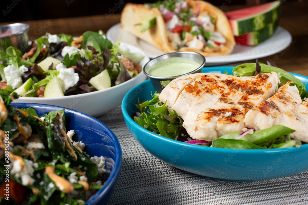 A view of several Californian Mediterranean fusion dishes on a table, featuring chicken and salads. A view of several Californian Mediterranean fusion dishes on a table, featuring chicken and salads.