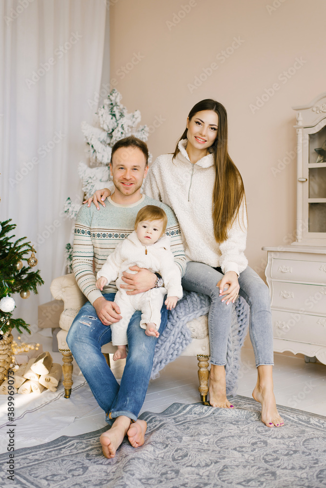 Stylish modern portrait of a young family with a small child. Happy close-knit family sitting near the Christmas tree on a chair