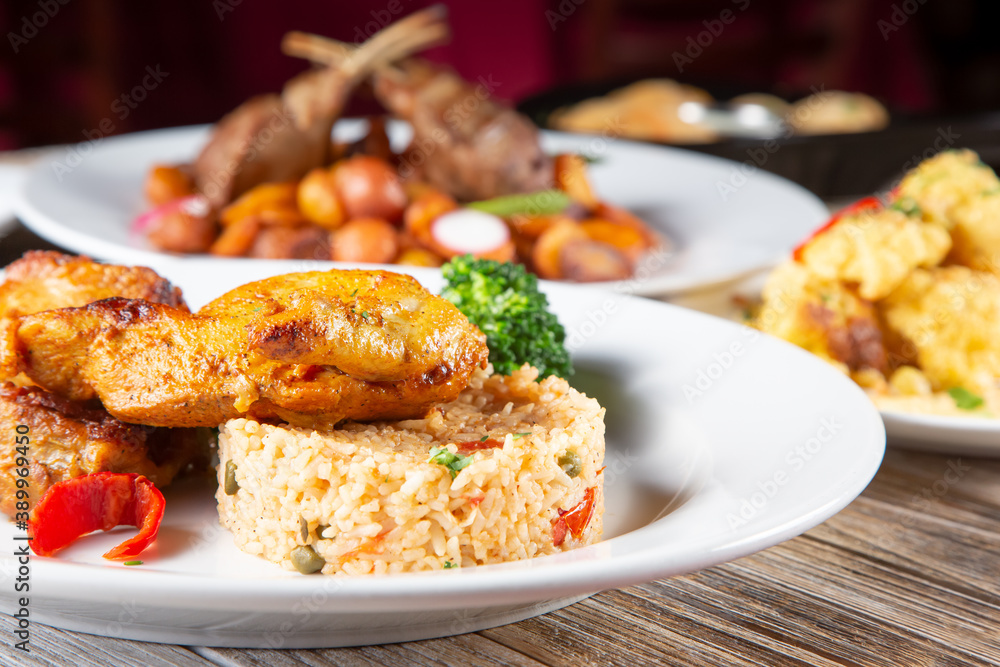 A view of a several entrees on a table, featuring roasted chicken and rice.