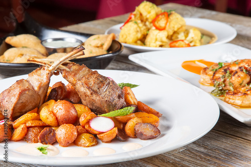 A view of several Spanish entrees on a table, featuring a plate of lamb chops and potatoes.