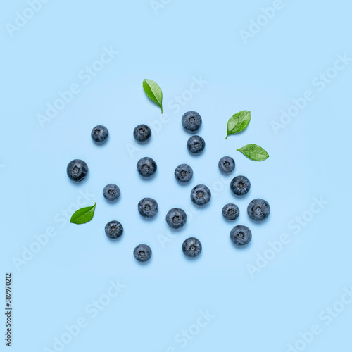 Fresh juicy blueberries with green leaves on blue background. Blueberries background. Flat lay top view copy space. Healthy berry, organic food, antioxidant, vitamin, blue food. Blueberry pattern