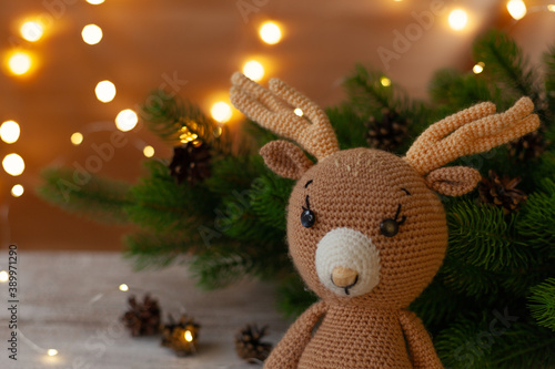 Wallpaper Mural close up knitted deer with antlers near a Christmas tree with cones, light garlands on a white wooden table. Torontodigital.ca