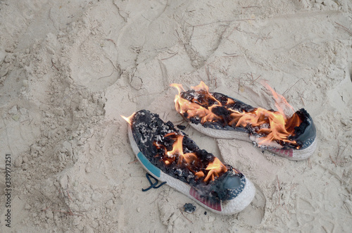 Burning sports sneakers or gym shoes on fire stand on sandy beach coast. Athlete burned out. Physical exertion during training concept photo