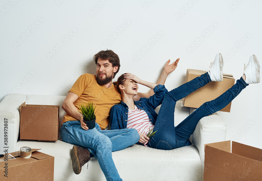 A man and a woman are sitting on the couch near the boxes with things moving the interior of the room
