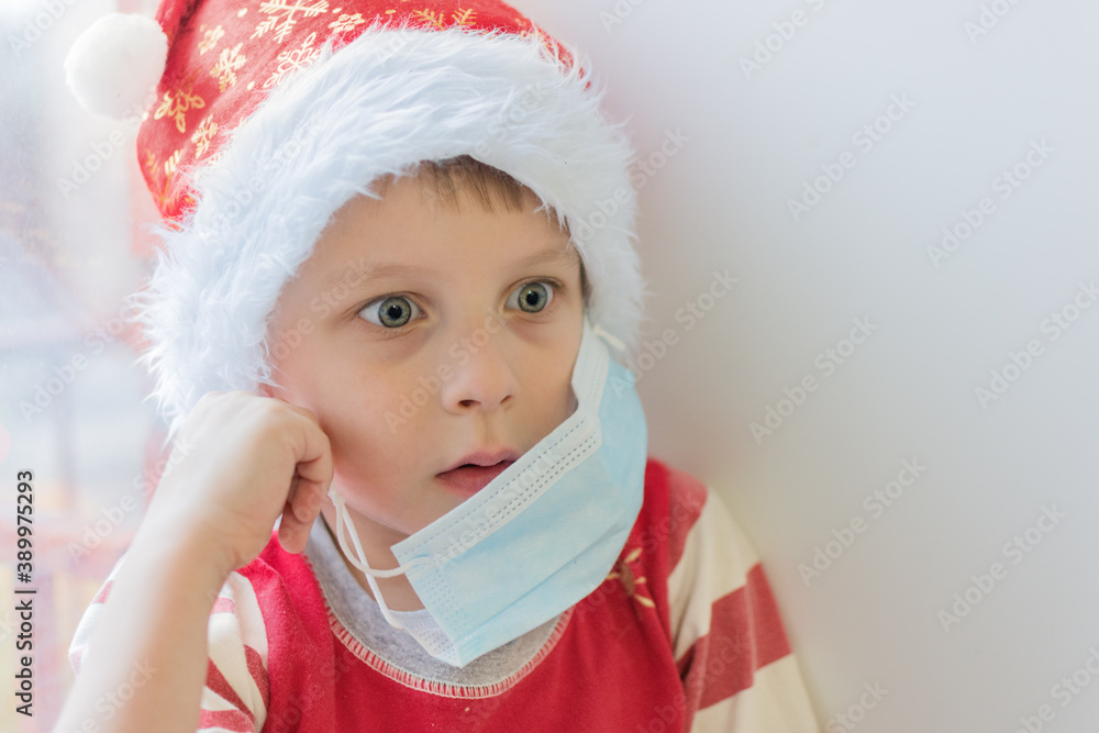 surprised boy in a santa hat takes off the medical mask. Close-up, soft focus, horizontal photo, without looking at the camera. End or tightening of isolation, bewilderment.