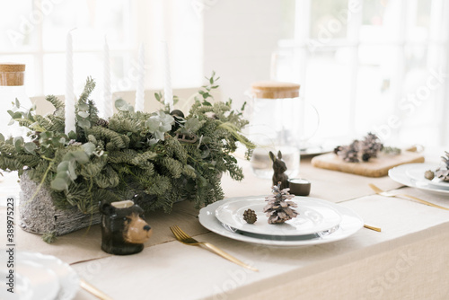 Stylish Christmas table setting: a composition of fir branches, white plates decorated with cones