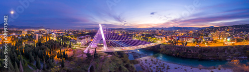 Illuminated Millennium bridge over Moraca river in Podgorica Montenegro, at night. 180 degrees panorama of the city under sunset sky with moon in it. photo