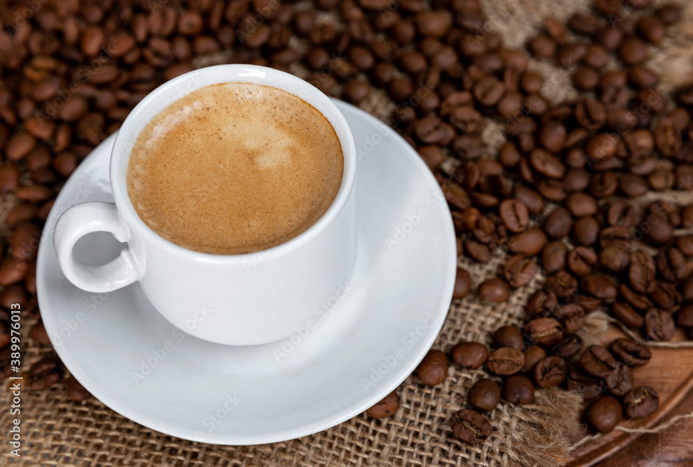 White cup of frothy coffee and sprinkled beans on sacking. Close-up. Top view. White cup of frothy coffee and sprinkled beans on sacking. Close-up. Top view.