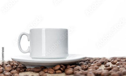 White cup with coffee on sprinkled roasted beans. White background. Space for text.
