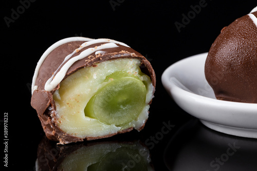 Chocolate truffle with green grape filling isolated on black background. Closeup photography. photo