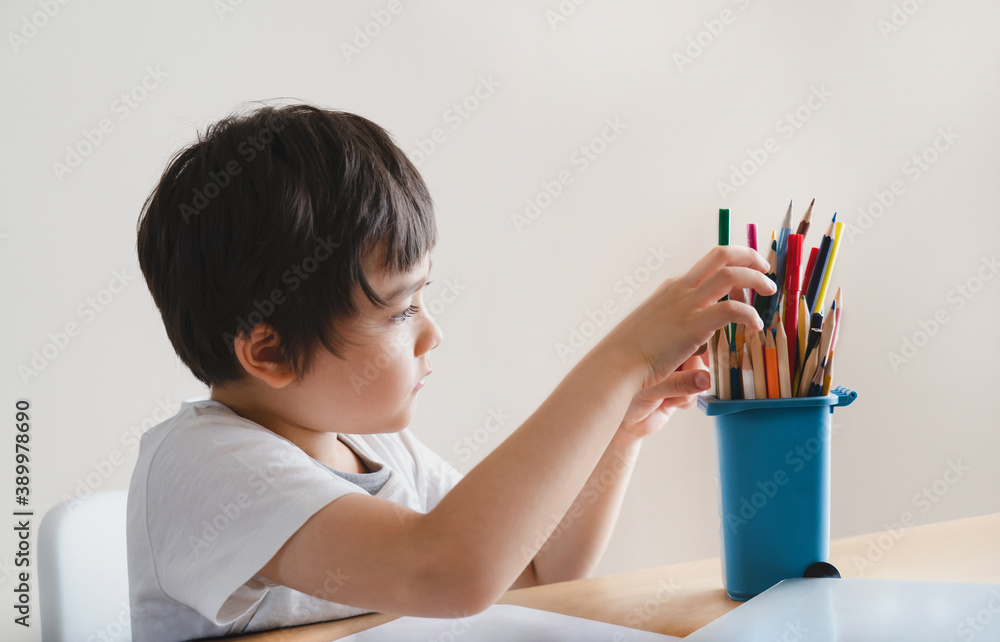 Active boy selecting his favorite pencil colour for painting,School kid using a pencils drawing on white paper, child relaxing at home,Home school,Distance education,E-learning,Self distancing concept Active boy selecting his favorite pencil colour for painting,School kid using a pencils drawing on white paper, child relaxing at home,Home school,Distance education,E-learning,Self distancing concept