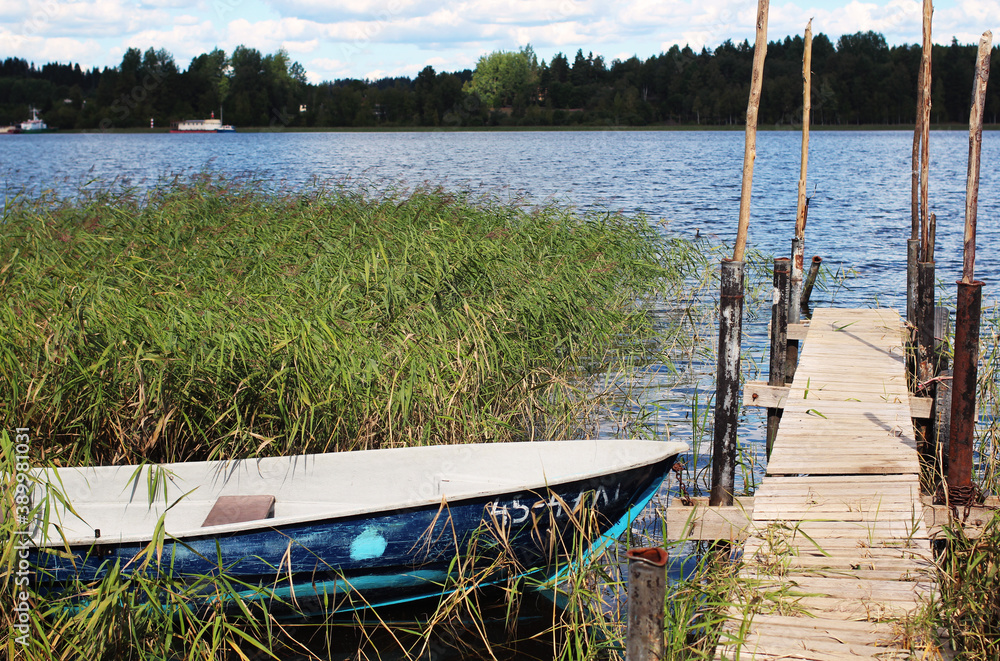 Fototapeta premium Blue boat near the pier on the river in the thickets of grass