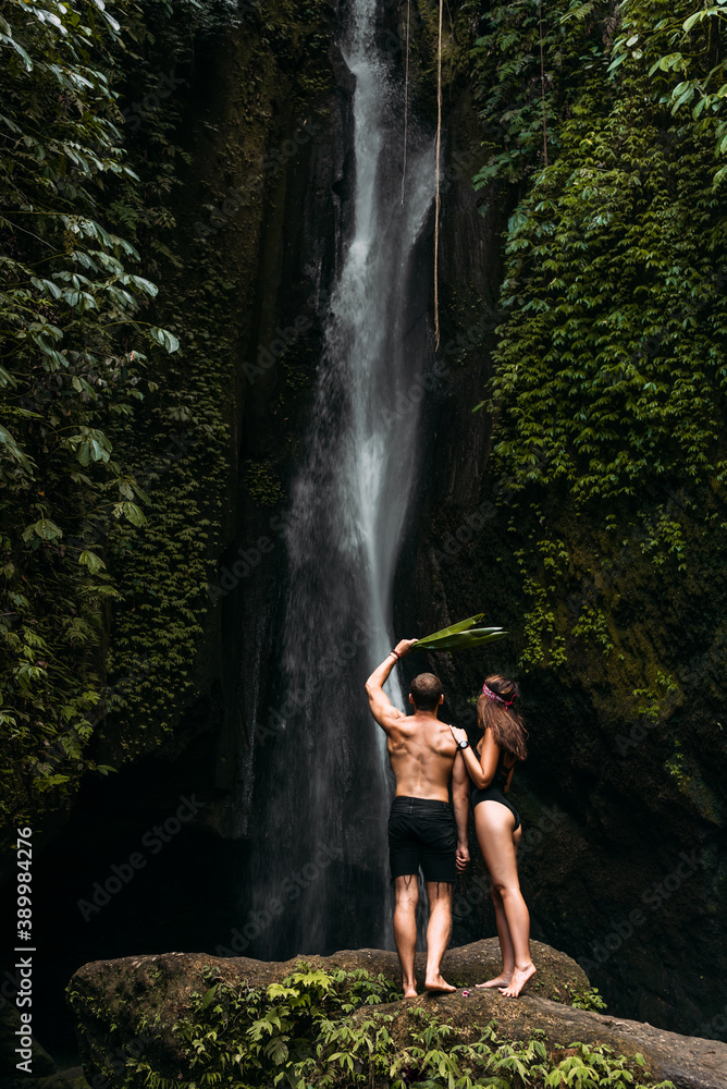 Tourists at the waterfall, rear view. Happy couple at a beautiful waterfall. Couple on vacation in Bali. Honeymoon trip. Vacation on the island of Bali. Tourists in Bali. Copy space
