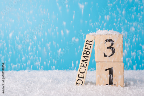 2021 is coming concept. Close up photo of wooden cube calender showing the last day of old year on snow falling background and blue bright color sky background