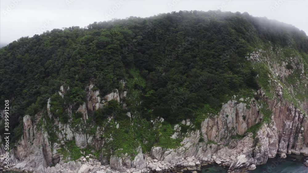 Flying above green forest of small Petrov island, a unique national reserve in Primorye, Russia. Aerial view of high rocky coast and wild wood Flying above green forest of small Petrov island, a unique national reserve in Primorye, Russia. Aerial view of high rocky coast and wild wood