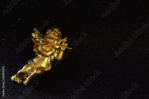 Golden angel on black shiny background, yellow glitter toy, Christmas decoration, place for text