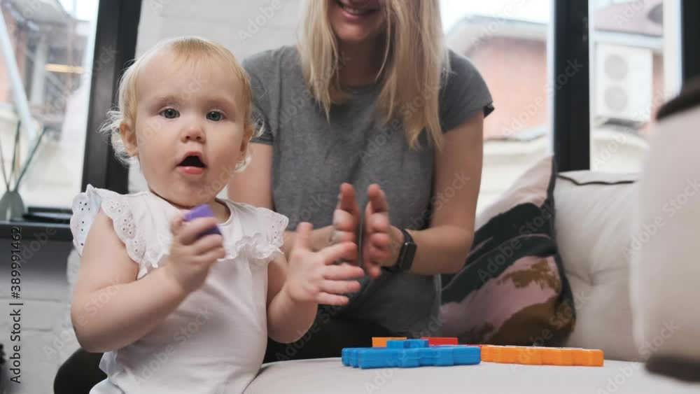 Mom and cute little daughter child play on the bed in colored cubes. The girl succeeds and she claps her hands. Mom and cute little daughter child play on the bed in colored cubes. The girl succeeds and she claps her hands.