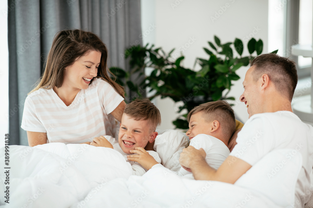 Young family enjoying in bed. Happy parents with sons relaxing in bed.. Young family enjoying in bed. Happy parents with sons relaxing in bed..