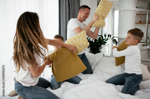 Young parents with sons fighting pillows on the bed. Happy mother and father with boys having fun at home. photo