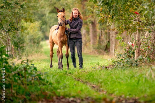 A light brown buckskin foal, the female owner stands next to the stallion Autumn Sun