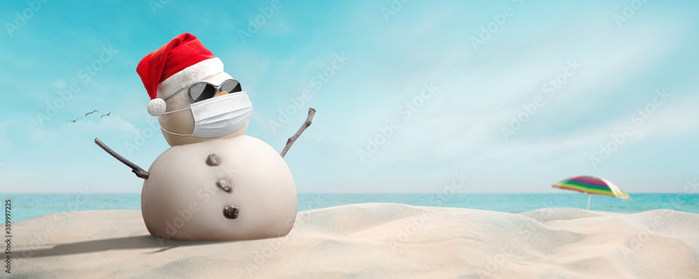 Concept: sand snowman wearing sunglasses, Santa hat and mask during coronavirus pandemic on sunny Christmas day afternoon COVID-19 - obrazy, fototapety, plakaty 