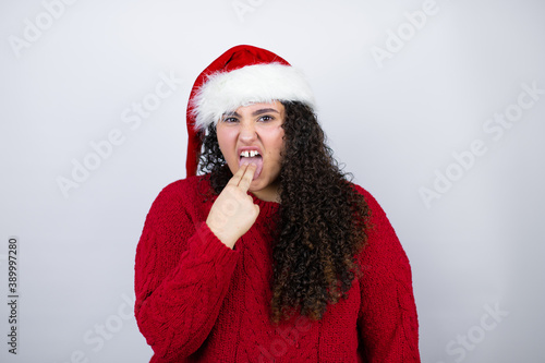 Young beautiful woman wearing a Santa hat over white background disgusted with her hand inside her mouth