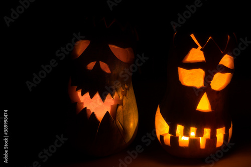 Two evil pumpkins for Halloween. An evil face is carved on the pumpkin, a candle is burning inside, in a dark room.