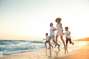 Happy family running on sandy beach near sea at sunset