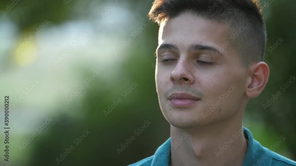 Optimistic brunet guy smiling and standing in a green park area in summer Optimistic brunet guy smiling and standing in a green park area in summer