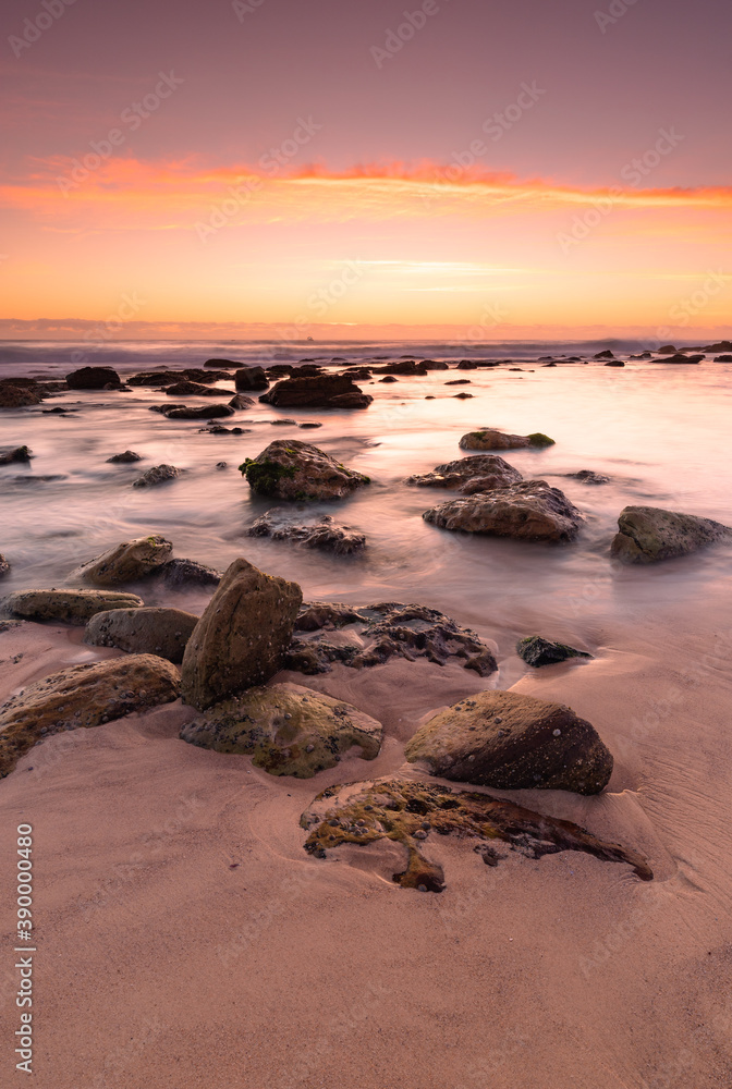 Sunrise at the ocean with rocks catching the first lights under magenta coloured sky.