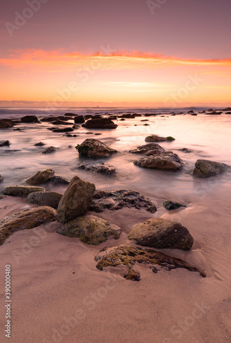 Sunrise at the ocean with rocks catching the first lights under magenta coloured sky.