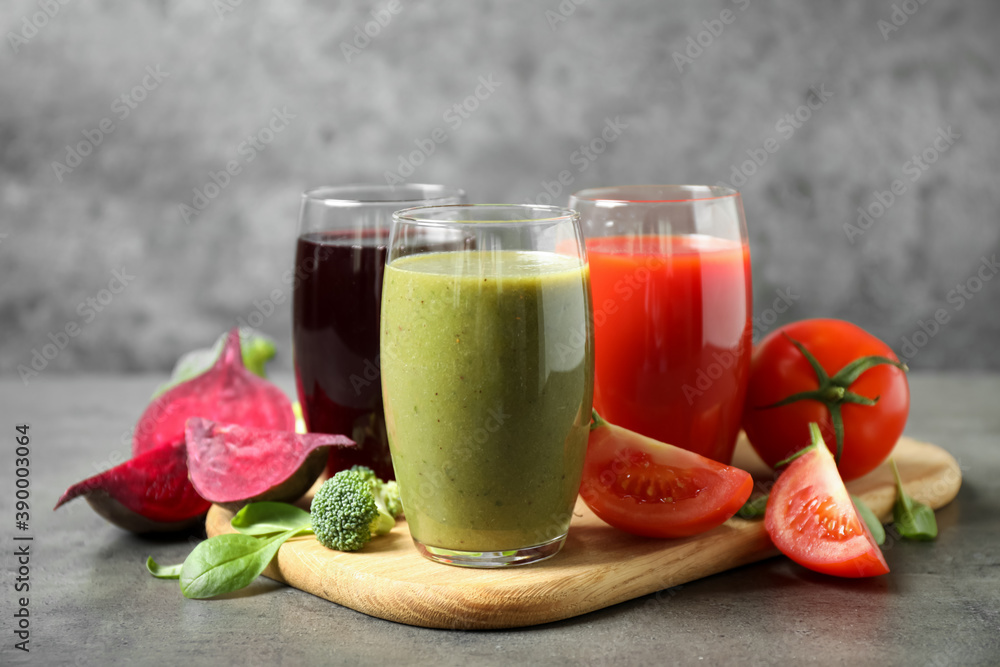 Delicious vegetable juices and fresh ingredients on grey table Delicious vegetable juices and fresh ingredients on grey table