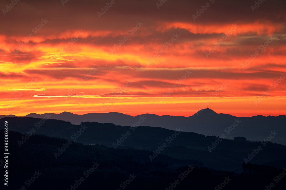 Coucher de soleil sur la Chaine des puys en Auvergne. Paysage touristique auvergnat. Du Puy de dôme jusqu'au Sancy. Montagnes et Panorama. Ciel rouge et nuageux lors du soleil couchant.
