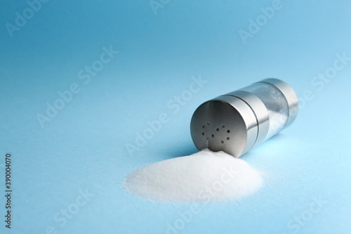 Scattered salt and shaker on light blue background, closeup. Space for text