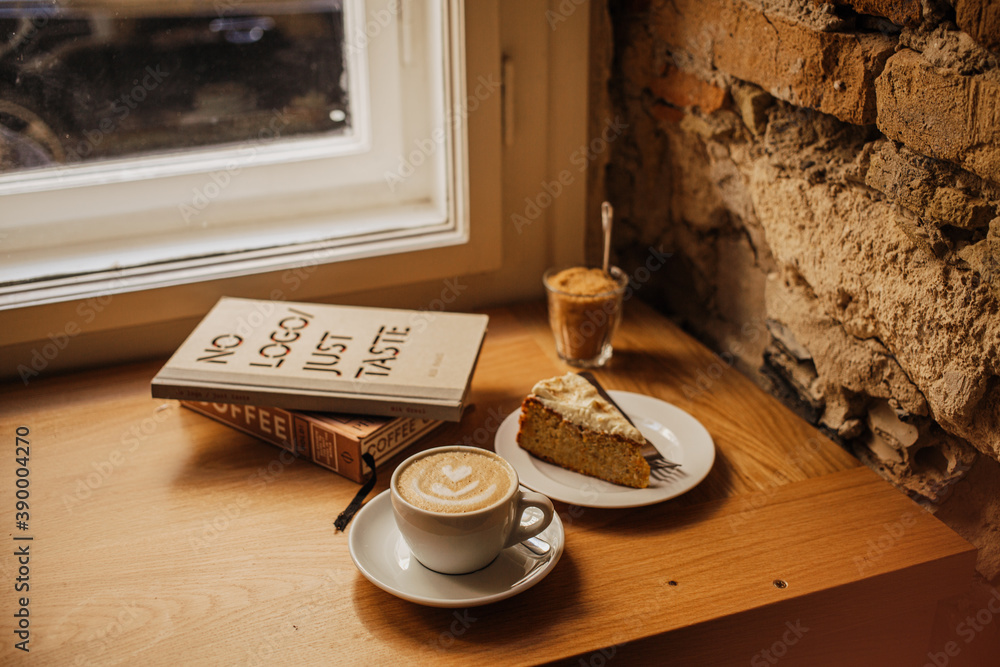 Obraz premium BUDAPEST, HUNGARY - Nov 03, 2019: Cup of coffee next to a piece of cake put on the windowsill