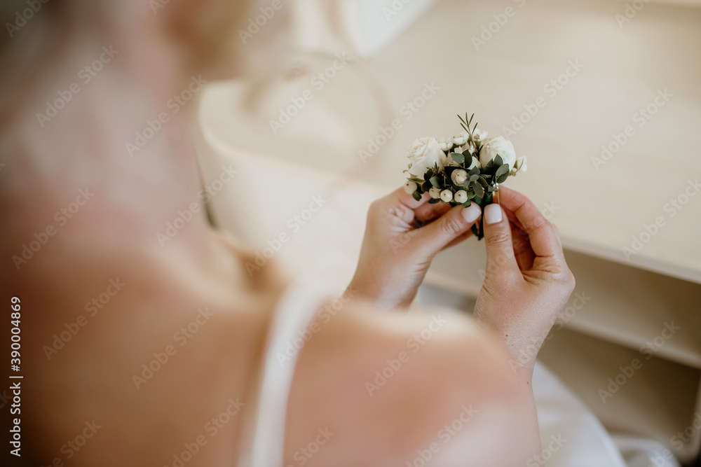 Obraz premium A beautiful bride sits on a chair and holds in her hands a decoration of flowers, which she will give and put on the jacket of the groom, her beloved man. Emphasis on hands and decoration