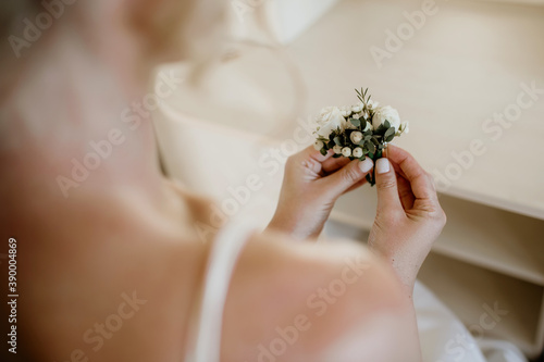 A beautiful bride sits on a chair and holds in her hands a decoration of flowers, which she will give and put on the jacket of the groom, her beloved man. Emphasis on hands and decoration