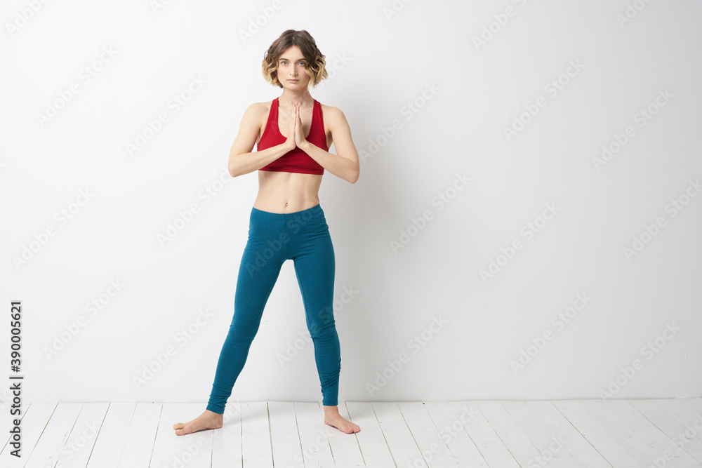 Fototapeta premium sports woman in a bright room doing yoga in full growth blue leggings and a red tank top