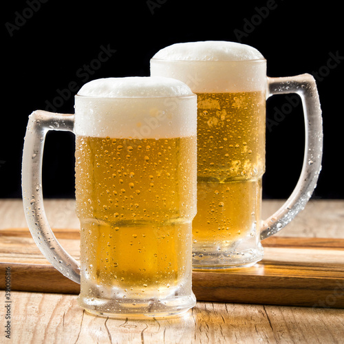 Canvas Print Two draft beer mugs on wooden table and black background