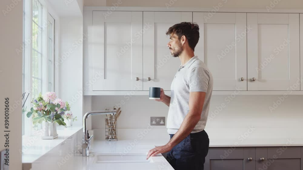 Morning shot of man standing by kitchen window relaxing with hot drink - shot in slow motion Morning shot of man standing by kitchen window relaxing with hot drink - shot in slow motion