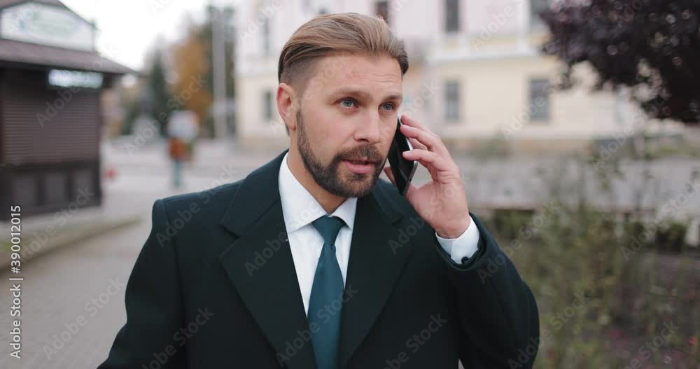 Successful businessman in formal outfit walking on street and talking on mobile. Bearded man having working conversation outdoors. Successful businessman in formal outfit walking on street and talking on mobile. Bearded man having working conversation outdoors.