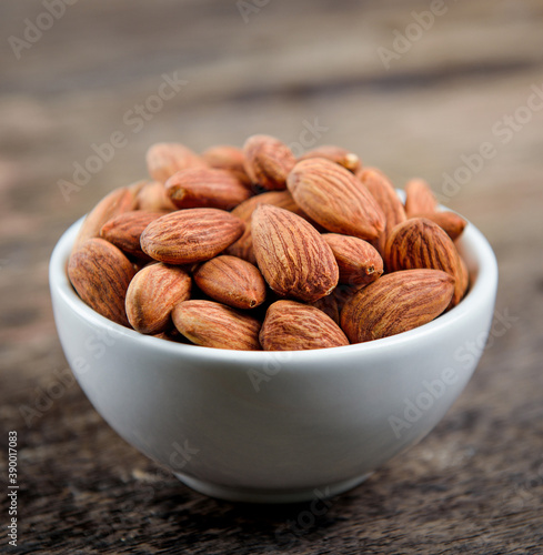 Almonds in white bowl on wooden table.