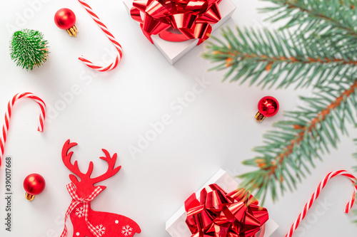 Happy holiday scene. White gift box with red ribbon, New Year balls and winter tree in Christmas composition on white background for greeting card. Xmas backdrop with space for text.