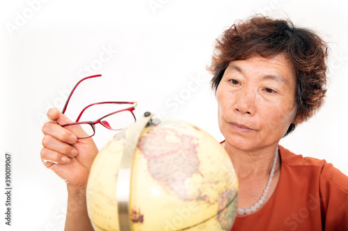 Фотография An old Chinese lady carefully looking at the globe in front of a white backgroun