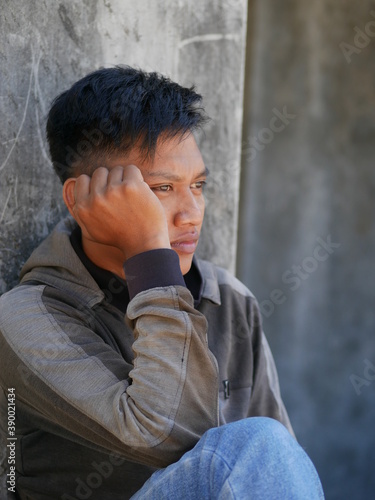 An Indonesian teenager boy worried sitting with a hand on the head. portrait of Asian young man depressed and sad.