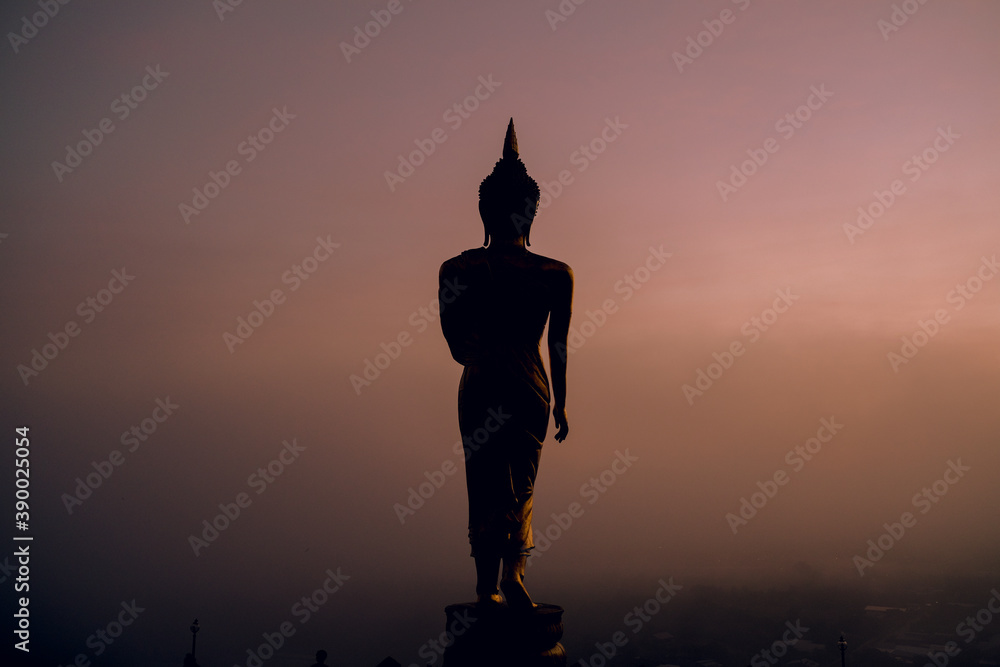 silhouette of big buddha in a standing position with the mist and sunlight morning at Wat Phrathat Khao Noi in Nan Province, north of Thailand. 
