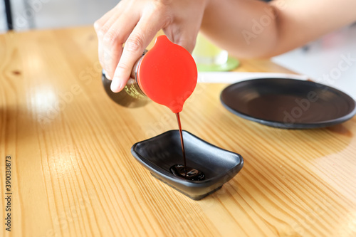 Hands are pouring black sauce on a cup in a Japanese restaurant.